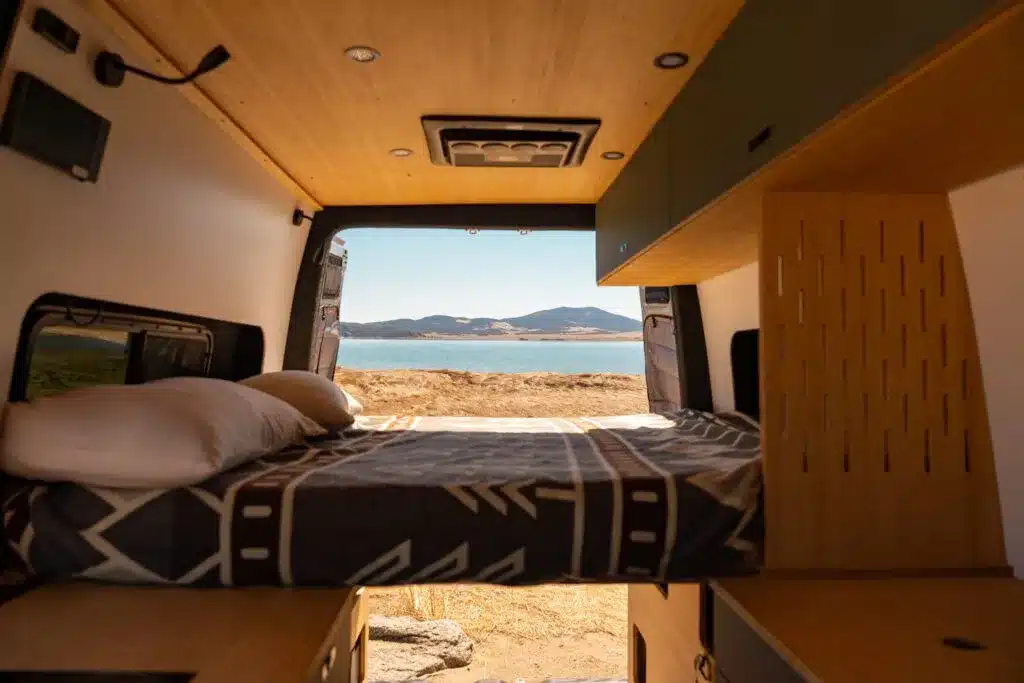 Innenraum eines Geotrek Convoy Campervans mit quer angeordnetem Bett und Holzmöbeln