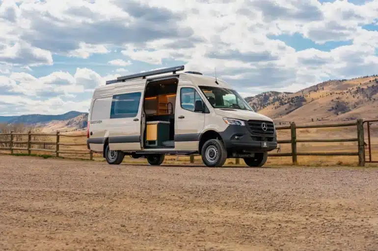 Weißer Geotrek Teton Campervan mit geöffneter Schiebetür vor einer Berglandschaft