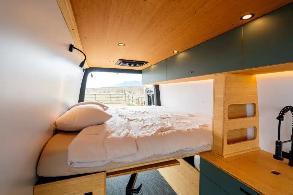 Innenraum eines Geotrek Teton Campervans mit großem Längsbett, Holzdach, Küchenzeile und Oberschränken