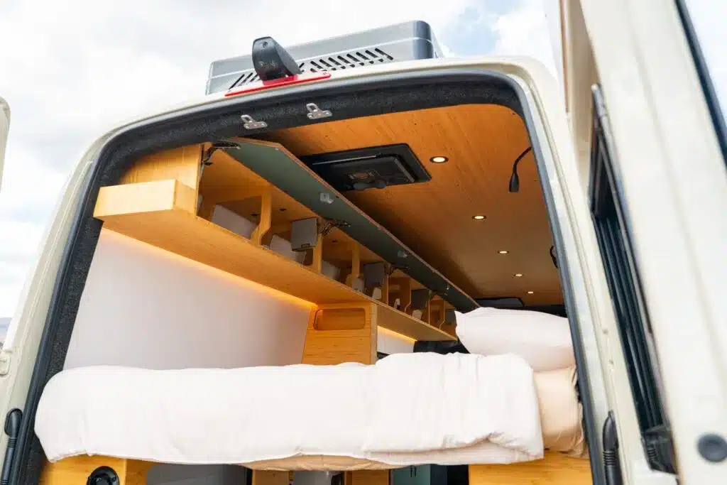 Innenraum eines Geotrek Teton Campervans mit weißem Längsbett, Holzdecke und Stauraum