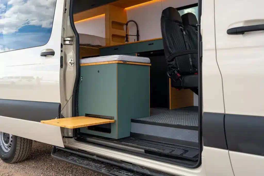 Innenraum des Geotrek Teton Campervans mit Küchenzeile, Spüle, Bett und ausklappbarem Tisch