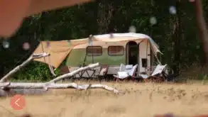 Wohnwagen mit ausgefahrenem Vorzelt, Campingmöbeln und Sitzbereich am Waldrand