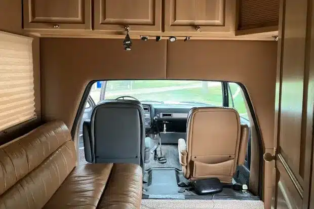Innenraum eines GMC C7000 Toterhome mit Ledersofa, Holzschränken und Durchgang zum Fahrerhaus