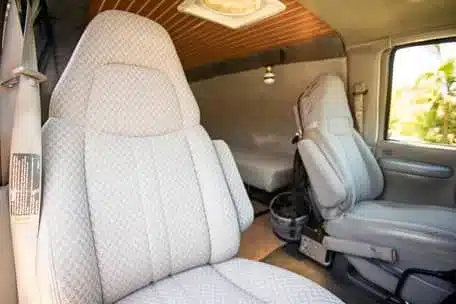 Innenraum eines GMC Savana G2500 mit hellen Vordersitzen, Holzdecke und Schlafbereich