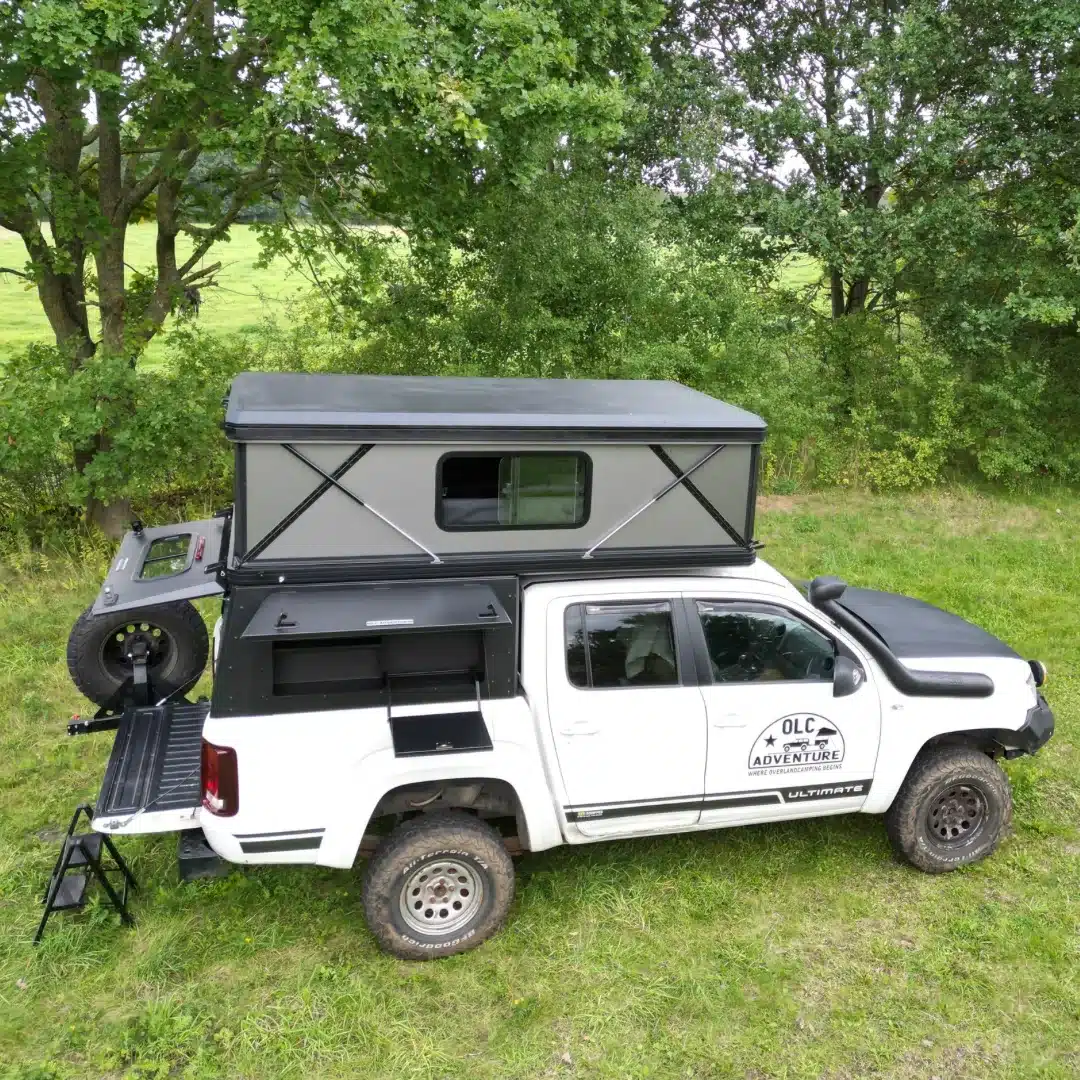 Weißer Pickup mit montiertem OLC Adventure Hardtop PickUp Camper und aufgebauter Schlafkabine im Grünen
