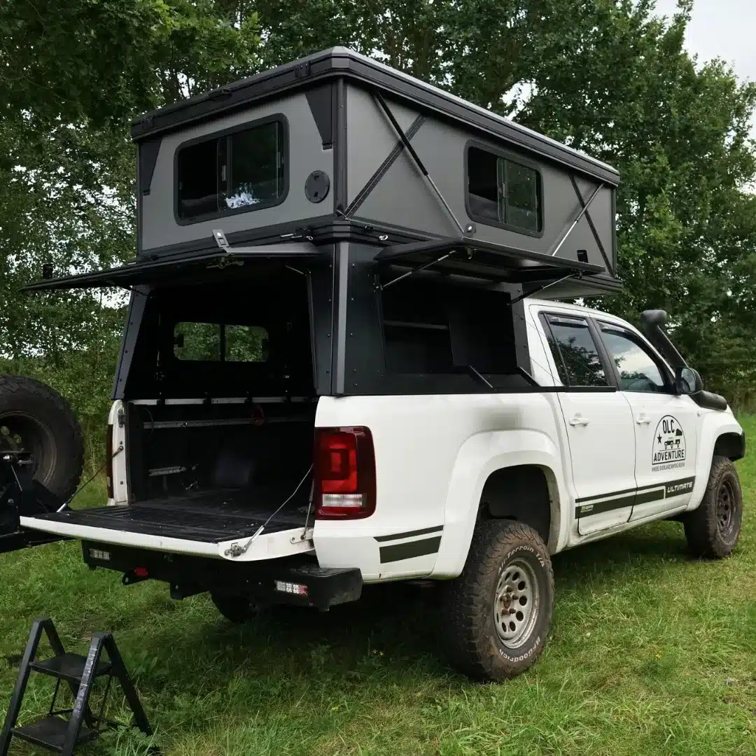 Weißer Pickup mit aufgebautem OLC Adventure Hardtop PickUp Camper und geöffneter Heckklappe im Grünen