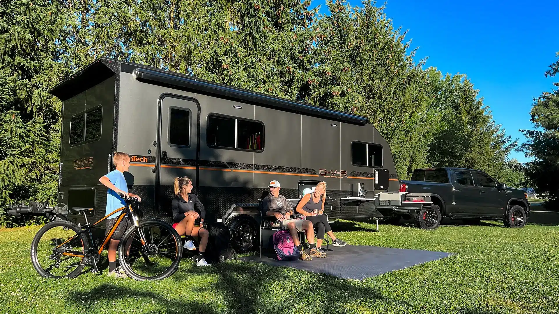 Schwarzer inTech O-V-R Navigate Wohnanhänger mit Markise, Fahrrädern und Familie auf einem Campingplatz