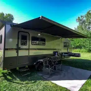 inTech O-V-R Navigate Travel Trailer mit ausgefahrener Markise, Sitzbereich und Fahrrad im Grünen