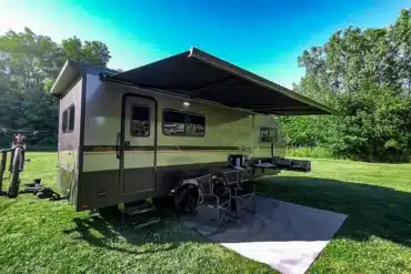inTech O-V-R Navigate Travel Trailer mit ausgefahrener Markise, Sitzbereich und Fahrrad im Grünen