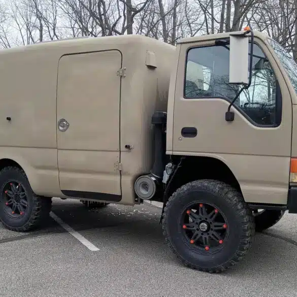 Beiger Isuzu NPR 4x4 Camper mit hohem Fiberglasaufbau auf einem Parkplatz