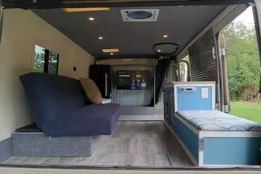 Innenraum des umgebauten Isuzu NPR 4x4 Campers mit Sofa, Bett und Fernseher