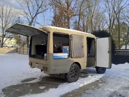 Beiger Isuzu NPR 4x4 Camper mit geöffneter Heckklappe und Seitentür im Schnee