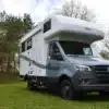 Weiß-graues Robel Mobil K 650 HLB auf Mercedes-Sprinter-Basis mit Alkoven steht auf einer Wiese vor einem Wald
