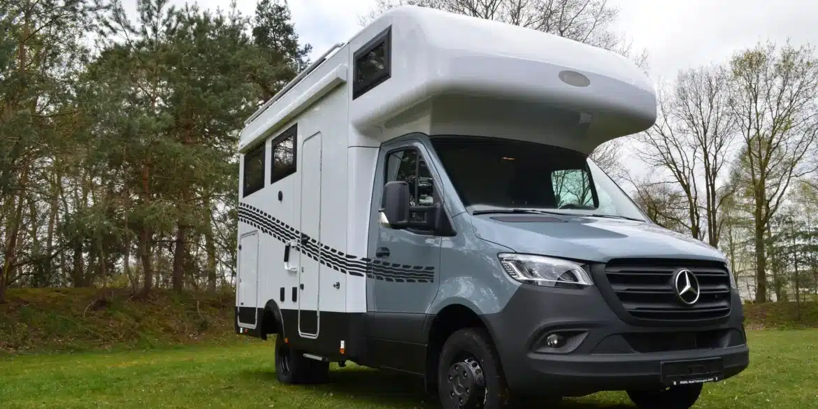 Weiß-graues Robel Mobil K 650 HLB auf Mercedes-Sprinter-Basis mit Alkoven steht auf einer Wiese vor einem Wald