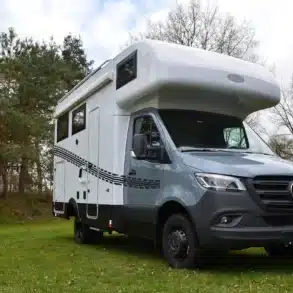 Weiß-graues Robel Mobil K 650 HLB auf Mercedes-Sprinter-Basis mit Alkoven steht auf einer Wiese vor einem Wald