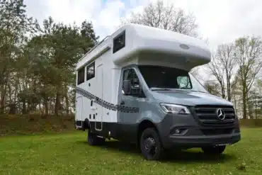 Weiß-graues Robel Mobil K 650 HLB auf Mercedes-Sprinter-Basis mit Alkoven steht auf einer Wiese vor einem Wald
