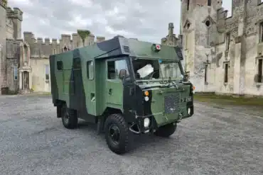 Grüner Land Rover 101 Forward Control Ambulance mit militärischem Aufbau und rotem Kreuz vor einem historischen Gebäude