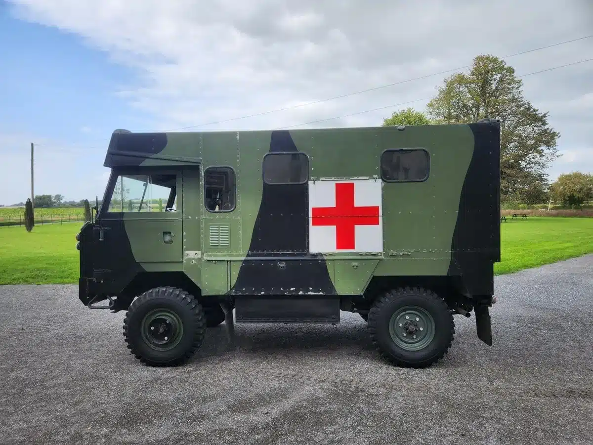 Grüner Land Rover 101 Forward Control Ambulance mit Tarnanstrich und rotem Kreuz auf einer Wiese
