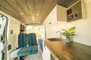 Innenraum des Mammoth Campervans mit Holzarbeitsplatte, Edelstahlspüle, weißen Wänden und drehbaren Vordersitzen