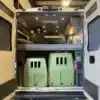 Heckbereich eines Campervans mit erhöhter Bettplattform und zwei grünen Hundeboxen darunter