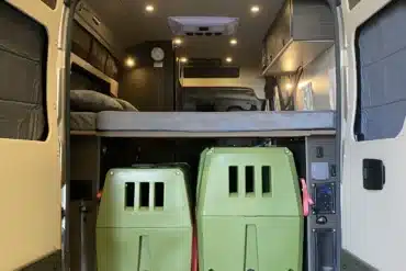 Heckbereich eines Campervans mit erhöhter Bettplattform und zwei grünen Hundeboxen darunter