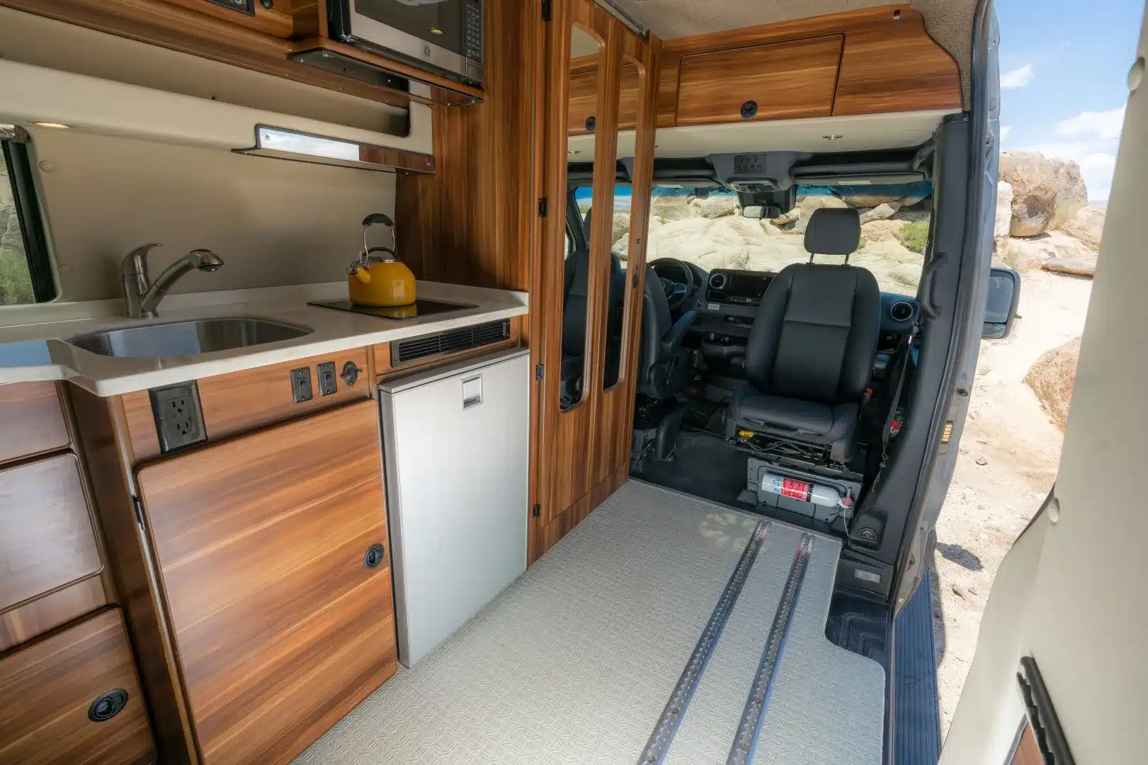 Innenraum des Millerton Campervans mit Holzküche, Spüle, Kühlschrank und Smartfloor-Schienen vor den Vordersitzen