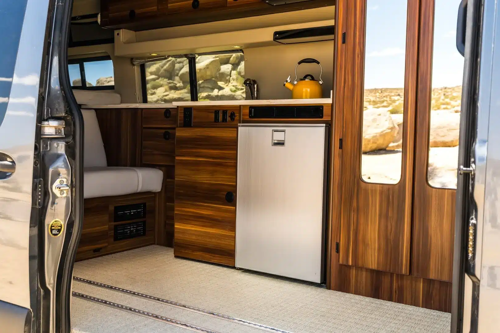 Innenansicht eines ausgebauten Millerton Campervans mit Holzküche, Kühlschrank, Sitzbank und Schienensystem im Boden