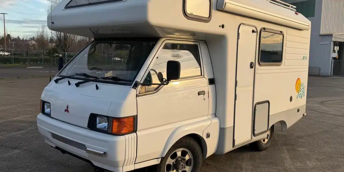 Weißer Mitsubishi Delica JB500 Camper in schräger Frontansicht mit Hochdach, Markise und Allradreifen