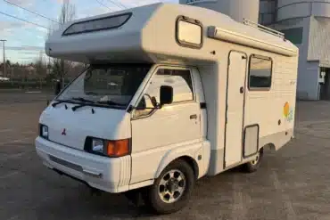 Weißer Mitsubishi Delica JB500 Camper in schräger Frontansicht mit Hochdach, Markise und Allradreifen