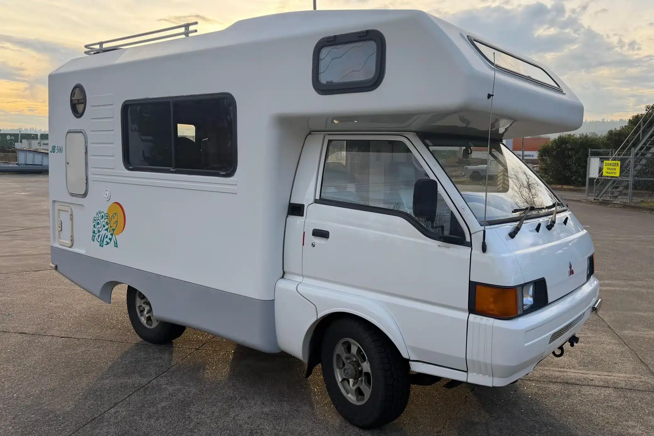 Weißer Mitsubishi Delica JB500 mit Allradantrieb, Camperkabine und Alkoven auf einem Parkplatz