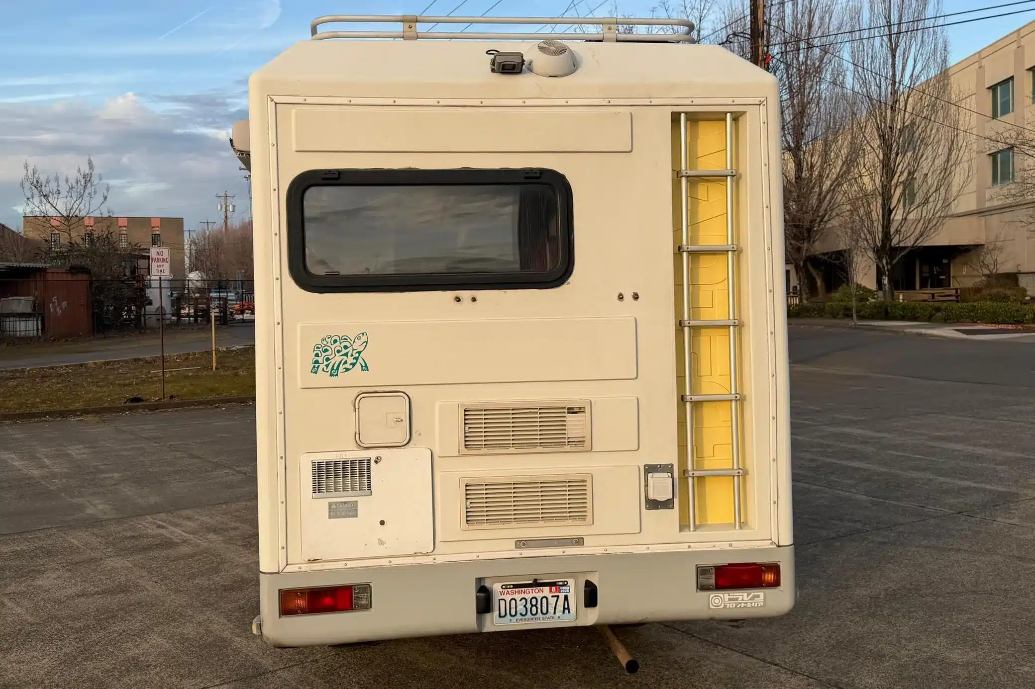 Heckansicht eines weißen Mitsubishi Delica JB500 mit Camperaufbau, Leiter und Dachgepäckträger