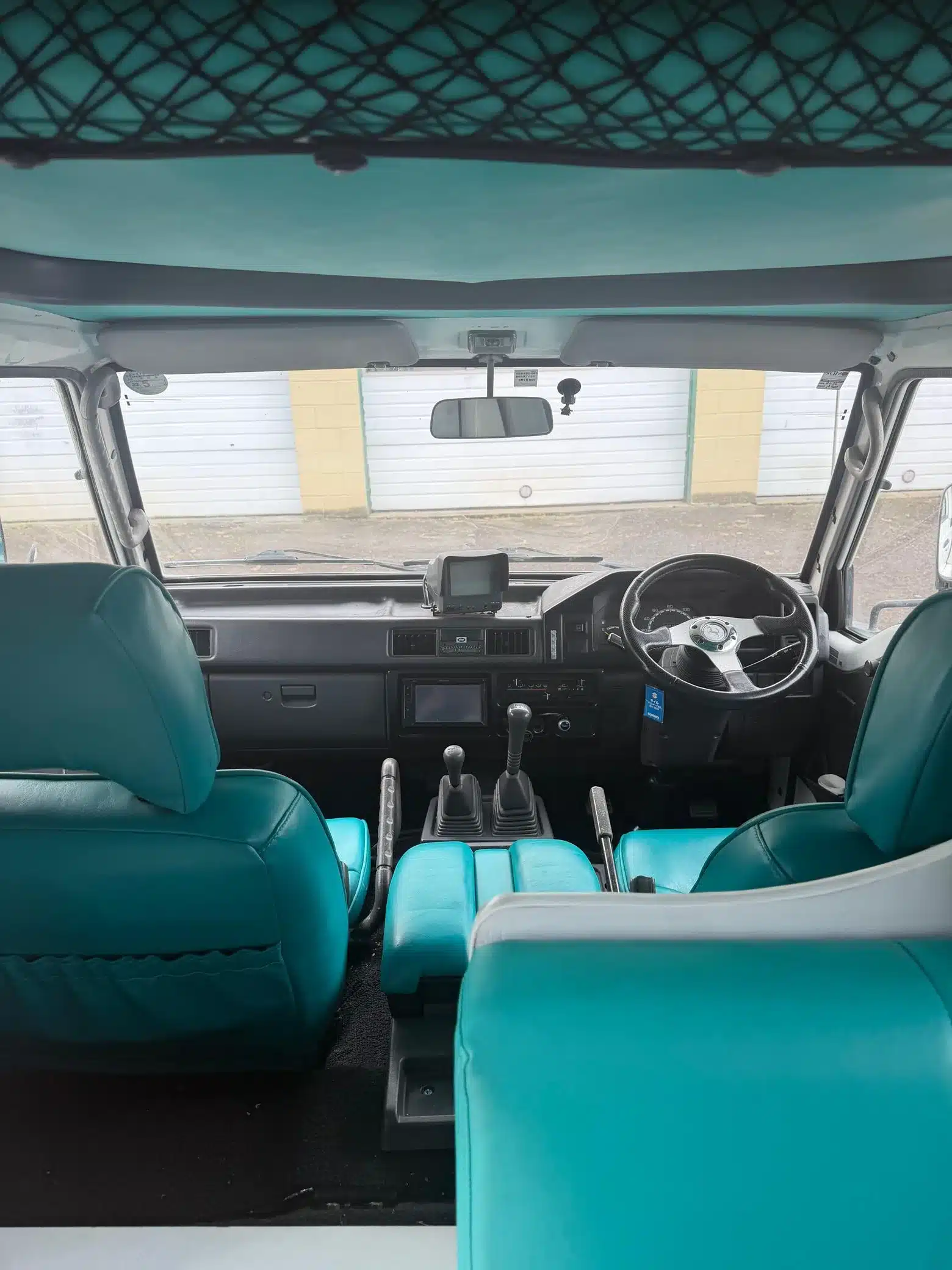 Innenansicht des Mitsubishi Delica JB500 mit türkisfarbenen Sitzen, Lenkrad rechts und zwei Schalthebeln