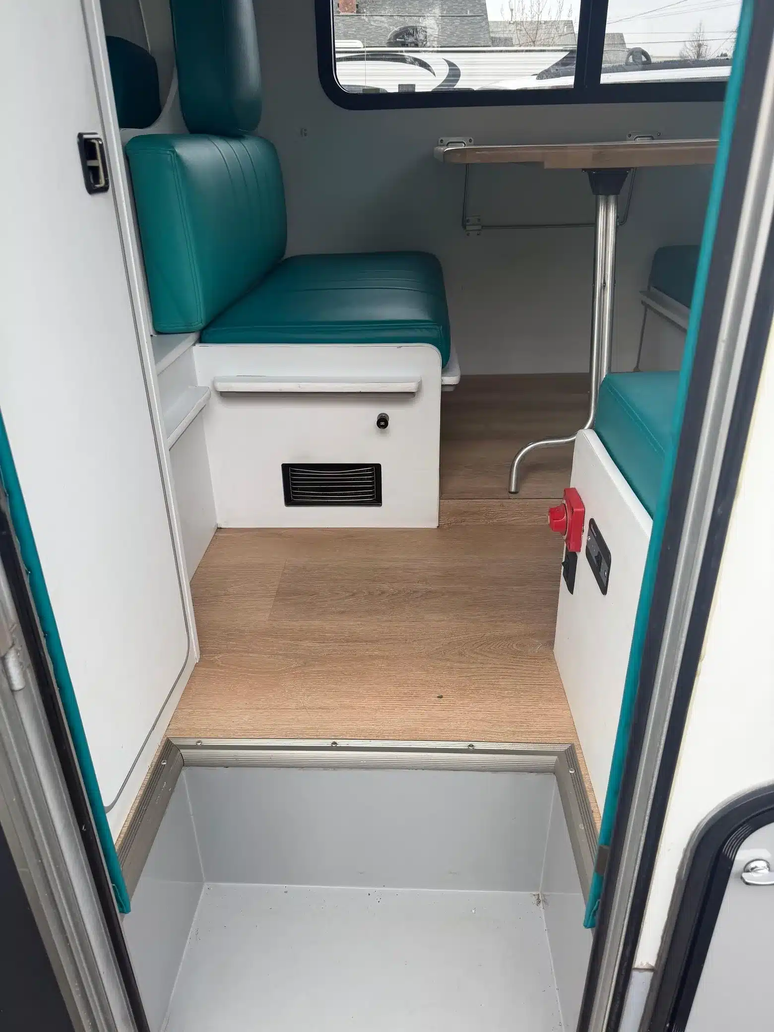 Innenraum des Mitsubishi Delica JB500 mit türkisfarbenen Polstersitzen, Klapptisch und Holzboden