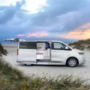 Weißer VW Transporter Camper mit geöffneten Türen und sichtbarem Innenausbau an einem Sandstrand