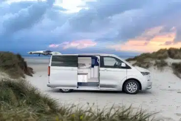 Weißer VW Transporter Camper mit geöffneten Türen und sichtbarem Innenausbau an einem Sandstrand