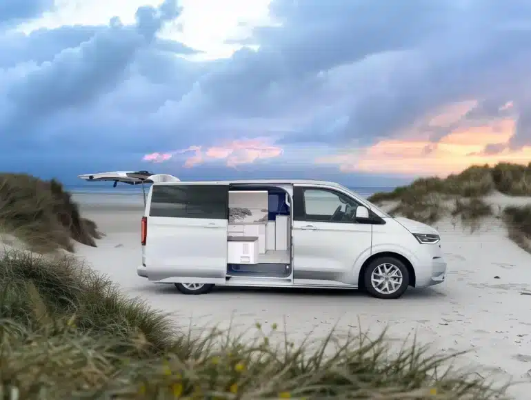 Weißer VW Transporter Camper mit geöffneten Türen und sichtbarem Innenausbau an einem Sandstrand