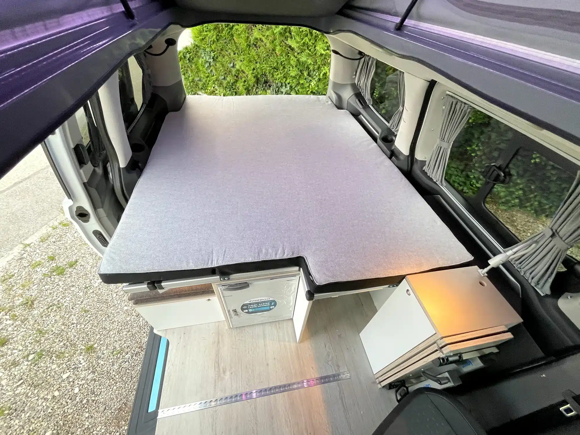 Innenraum eines VW Transporter Campers mit großem Bett, Küchenmodul und Holzfußboden