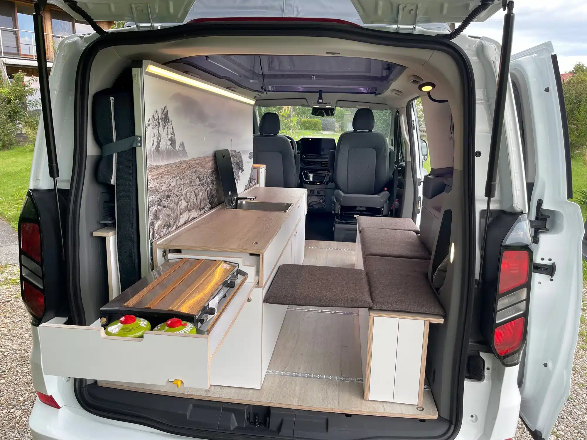 Innenraum eines weißen VW Transporter Camper mit Küchenmodul, Sitzbank und Wohnraumausbau