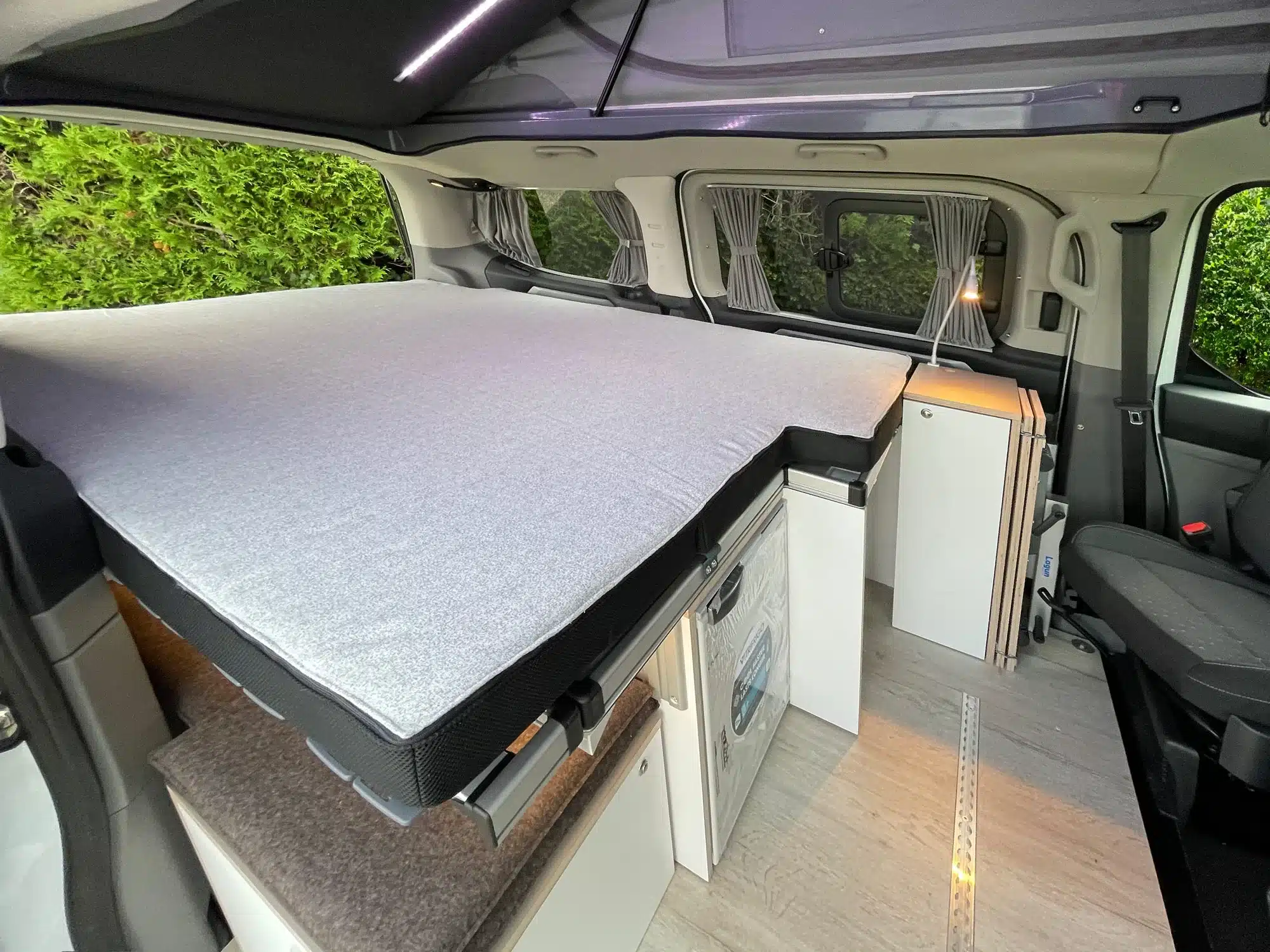 Innenraum eines VW Transporter Campers mit großem Bett, Küchenmodul und Mittelgang