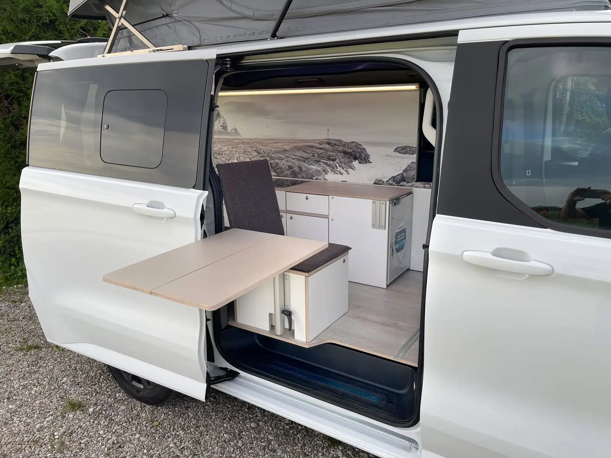 Innenansicht eines weißen New VW Transporter Campers mit Küchenmodul, Tisch und geöffnetem Aufstelldach