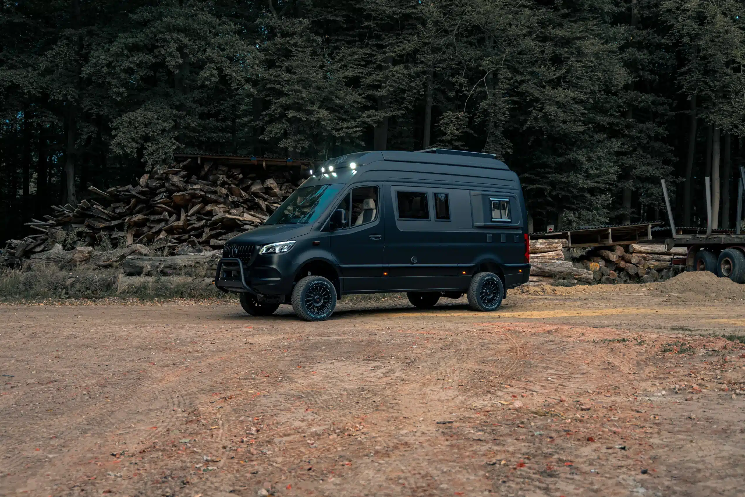 Dunkler geländegängiger Camper vor einem Wald auf unbefestigtem Untergrund