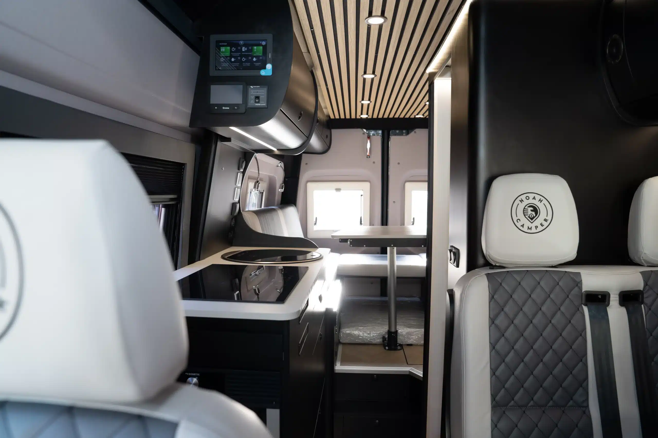 Innenraum des Noah Camper Pulse mit Sitzgruppe, Tisch, Schränken und digitalen Steuerpanelen für die Bordtechnik