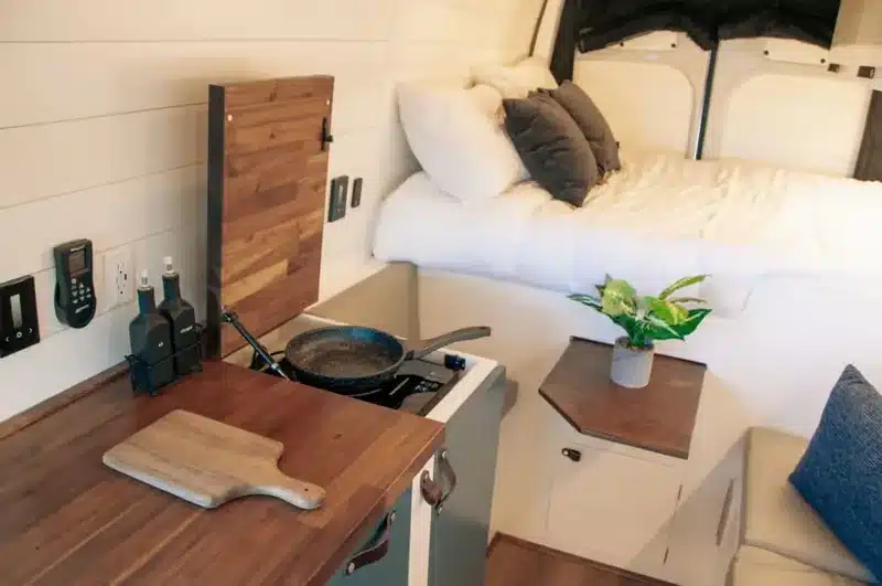 Innenraum eines ausgebauten Off-Grid-Vans mit Holzküche, Kochfeld, Sitzbank und Bett