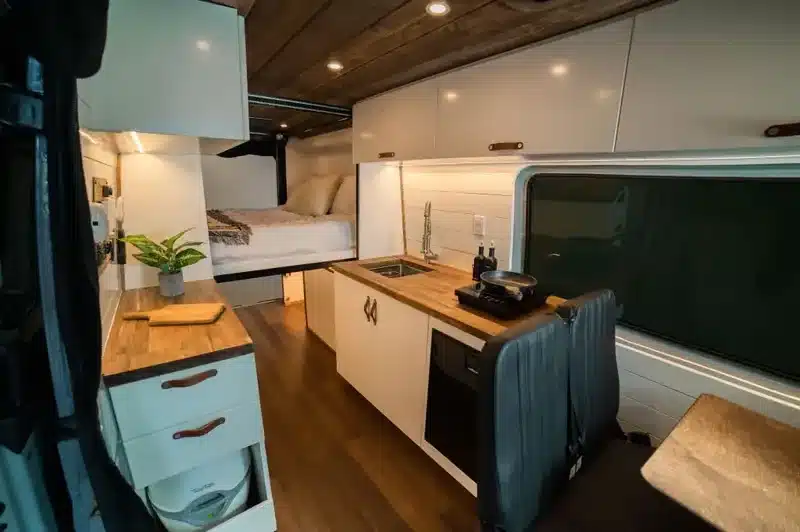 Innenraum eines ausgebauten Off-Grid-Vans mit Küche, Holzarbeitsplatte, Spüle, Kochfeld und Schlafbereich