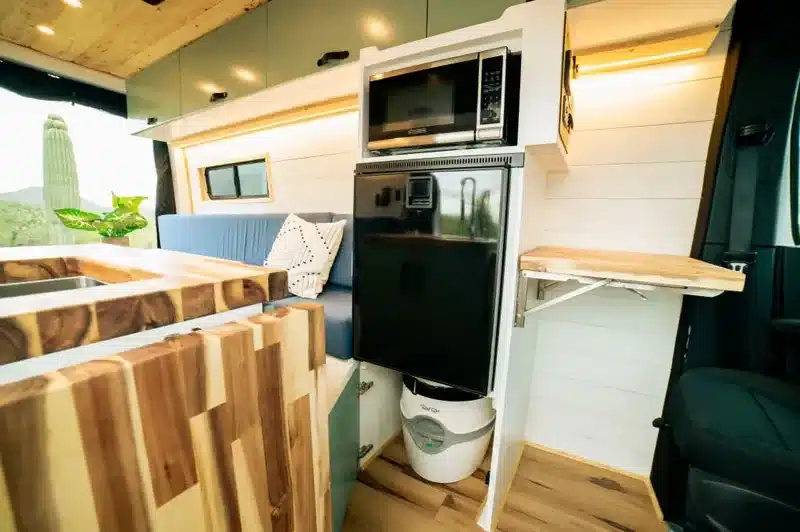 Innenraum eines ausgebauten Off-Grid-Vans mit Holzküche, Kühlschrank, Mikrowelle und kompakter Toilette