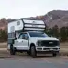 Weißer Full-Size-Pick-up mit aufgesetztem Outpost 6.5 Truck-Camper in einer Berglandschaft