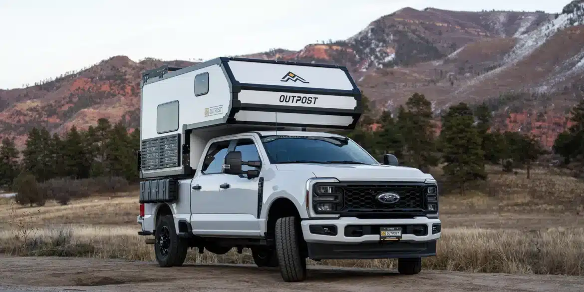 Weißer Full-Size-Pick-up mit aufgesetztem Outpost 6.5 Truck-Camper in einer Berglandschaft