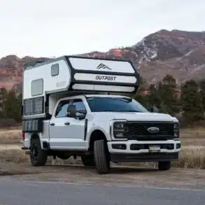 Weißer Full-Size-Pick-up mit aufgesetztem Outpost 6.5 Truck-Camper in einer Berglandschaft
