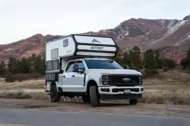 Weißer Full-Size-Pick-up mit aufgesetztem Outpost 6.5 Truck-Camper in einer Berglandschaft