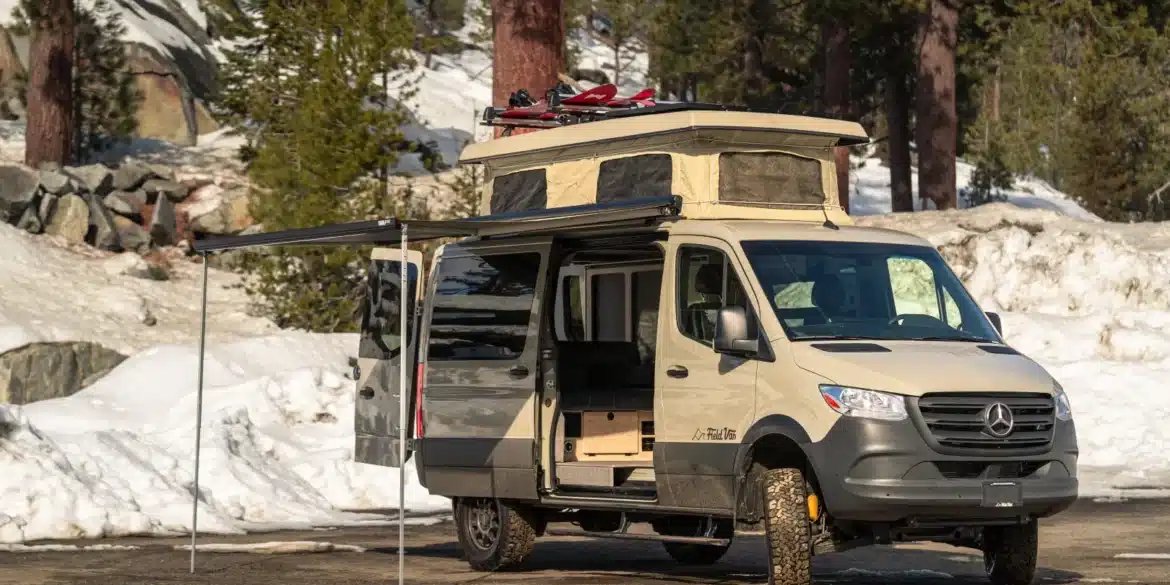 Campervan auf Mercedes-Benz-Sprinter-Basis mit Aufstelldach, Markise und Skiern im Schnee